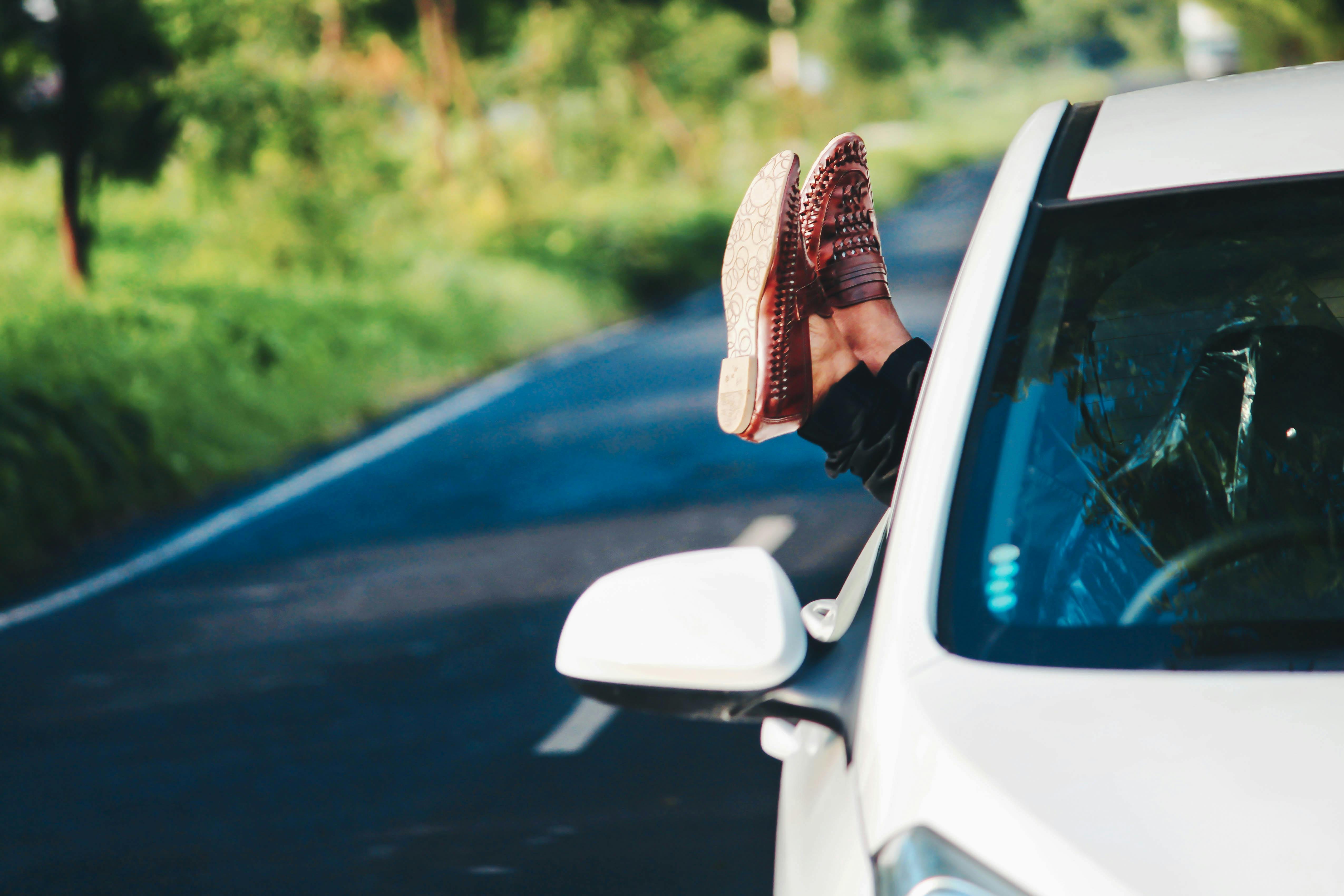 A person wearing loafers sticks their feet out of a car while on the road.